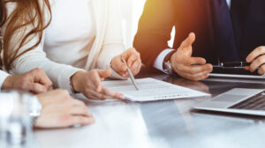 Business people discussing contract while working together in sunny modern office. Unknown businessman and woman with colleagues or lawyers at meeting.