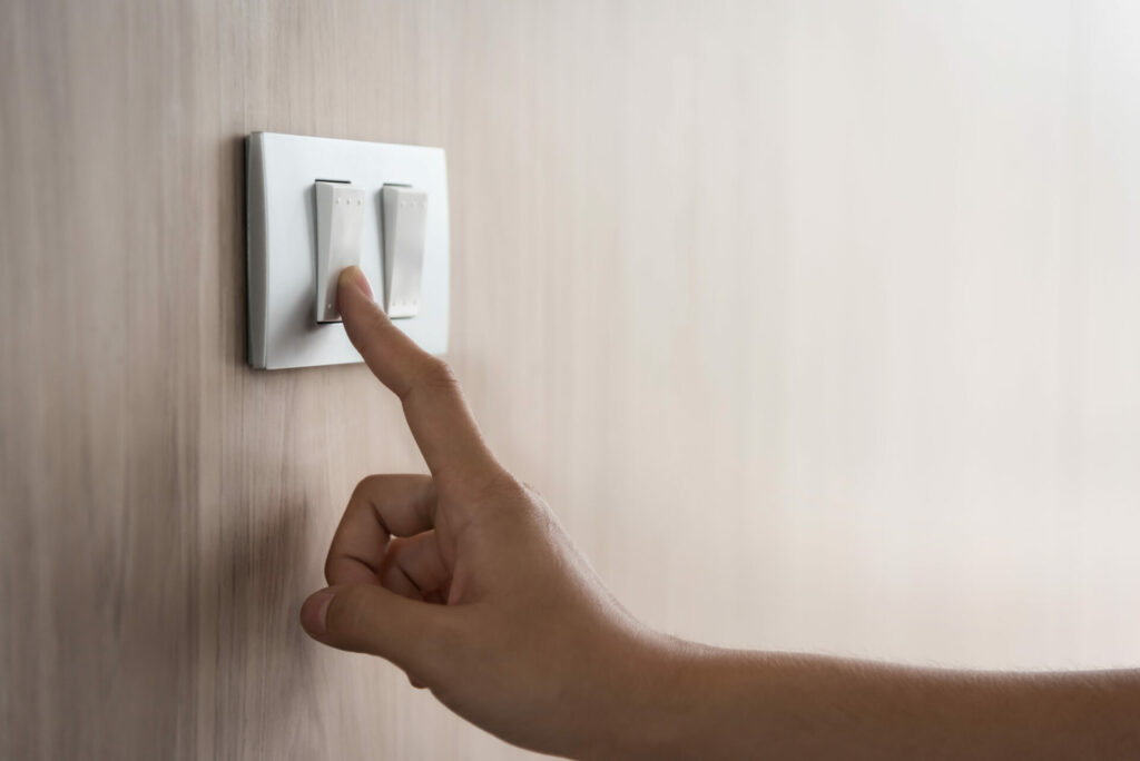 Close up hand turning on or off on grey light switch with wooden background.