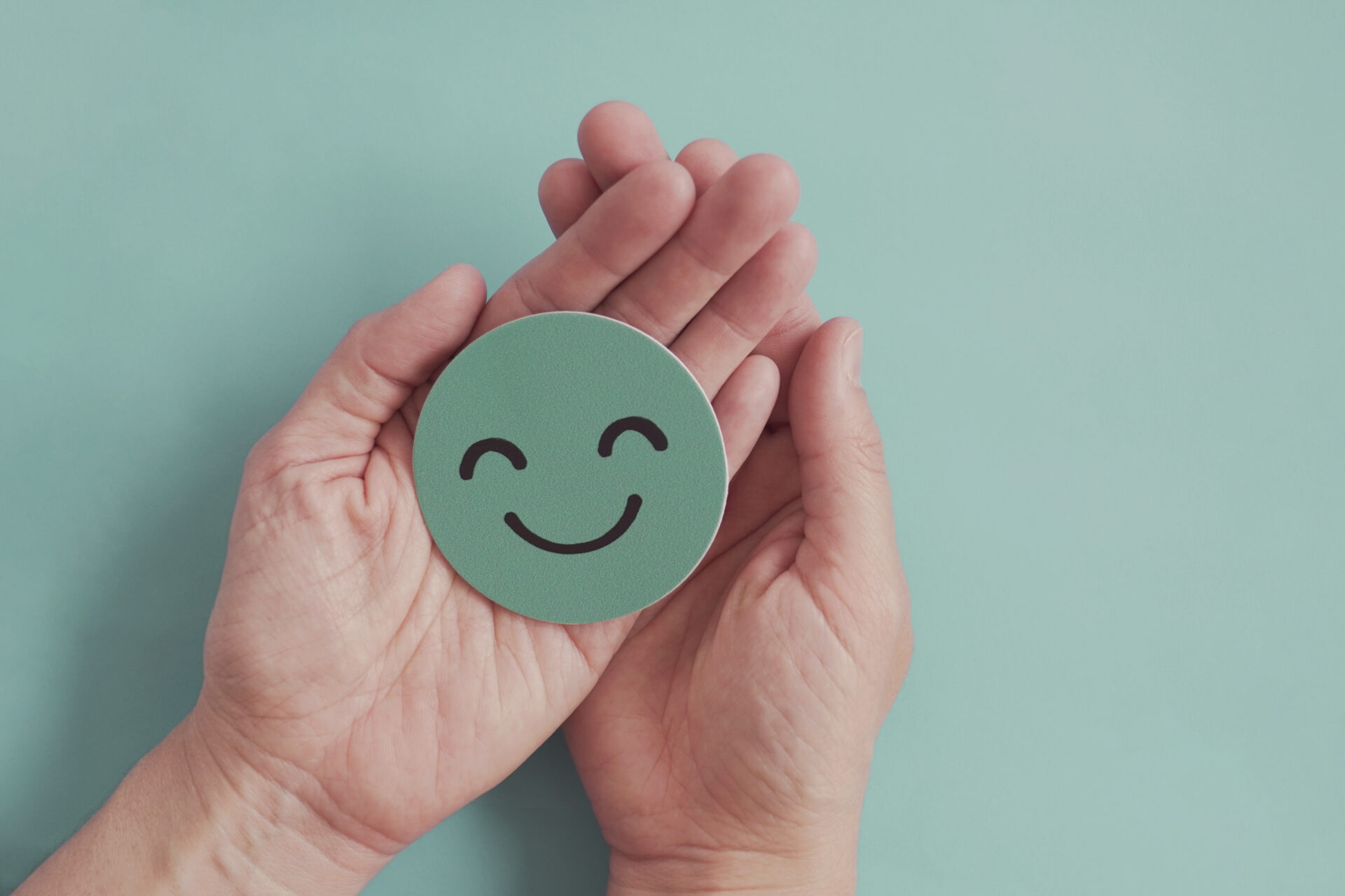 Hands holding green happy smile face paper cut out