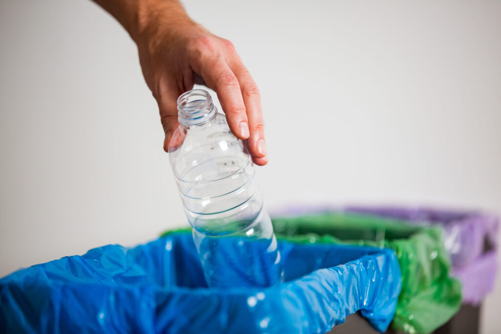 Hand putting single-use plastic bottle into recycling bin for simpler recycling.