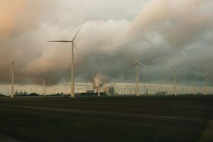 wind mills with smoke billowing behind them in the distance, representing carbon emissions trading systems [ets]