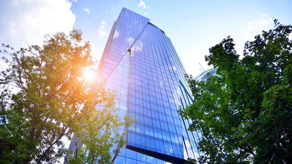 Sustainable glass office building with trees for reducing carbon dioxide. Eco-friendly building in modern city. Office with green environment. Corporate building reduce CO2.