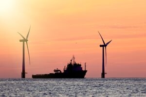 Ship near offshore wind turbines at sunset representing clean energy investment