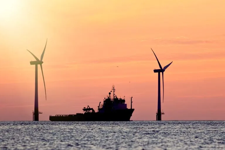 Ship near offshore wind turbines at sunset representing clean energy investment
