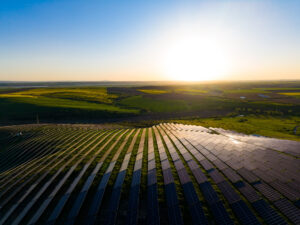 Solar panels cover a large area in the countryside as the sun sets in the background representing low fossil fuel generation