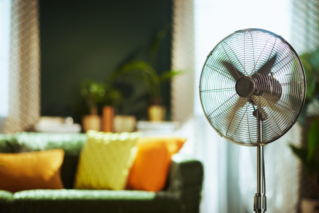 A modern stand fan with spinning blades is prominently featured in a comfortable living room representing climate change