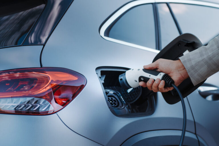 A man holding power supply cable at electric vehicle EV charging station, closeup representing ev sales