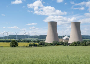 Green landscape and nuclear power plant against blue sky representing increase in nuclear jobs