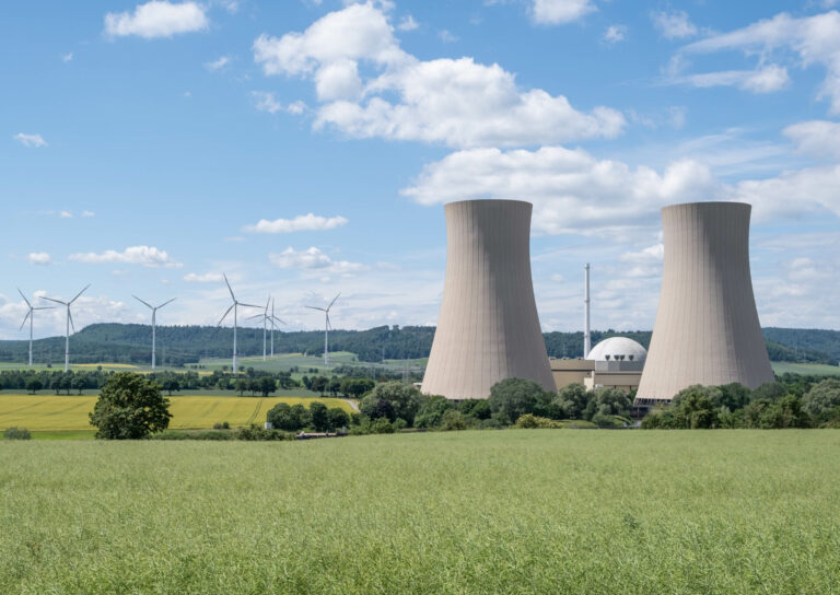 Green landscape and nuclear power plant against blue sky representing increase in nuclear jobs